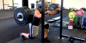Man performing a barbell Bulgarian split squat in a gym rack