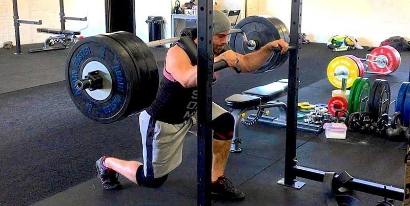 Man performing a barbell Bulgarian split squat in a gym rack