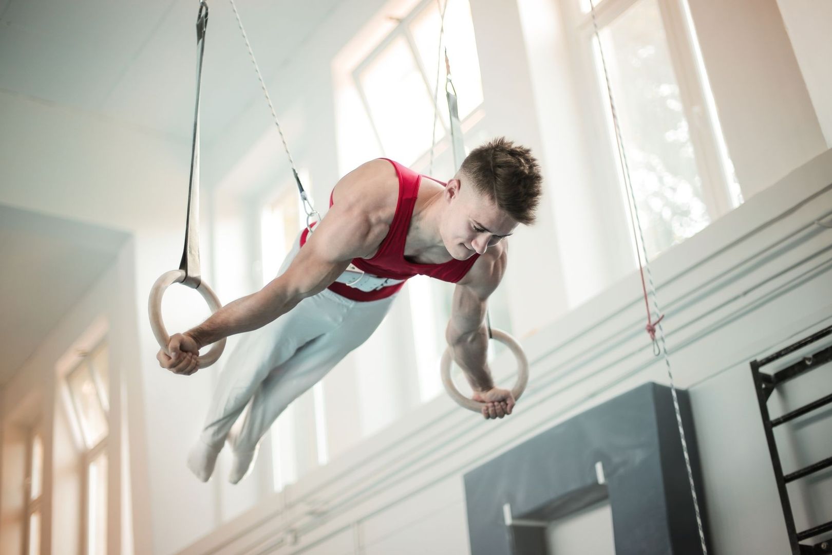 Gymnast holds a rigid body position on suspended rings in a gym